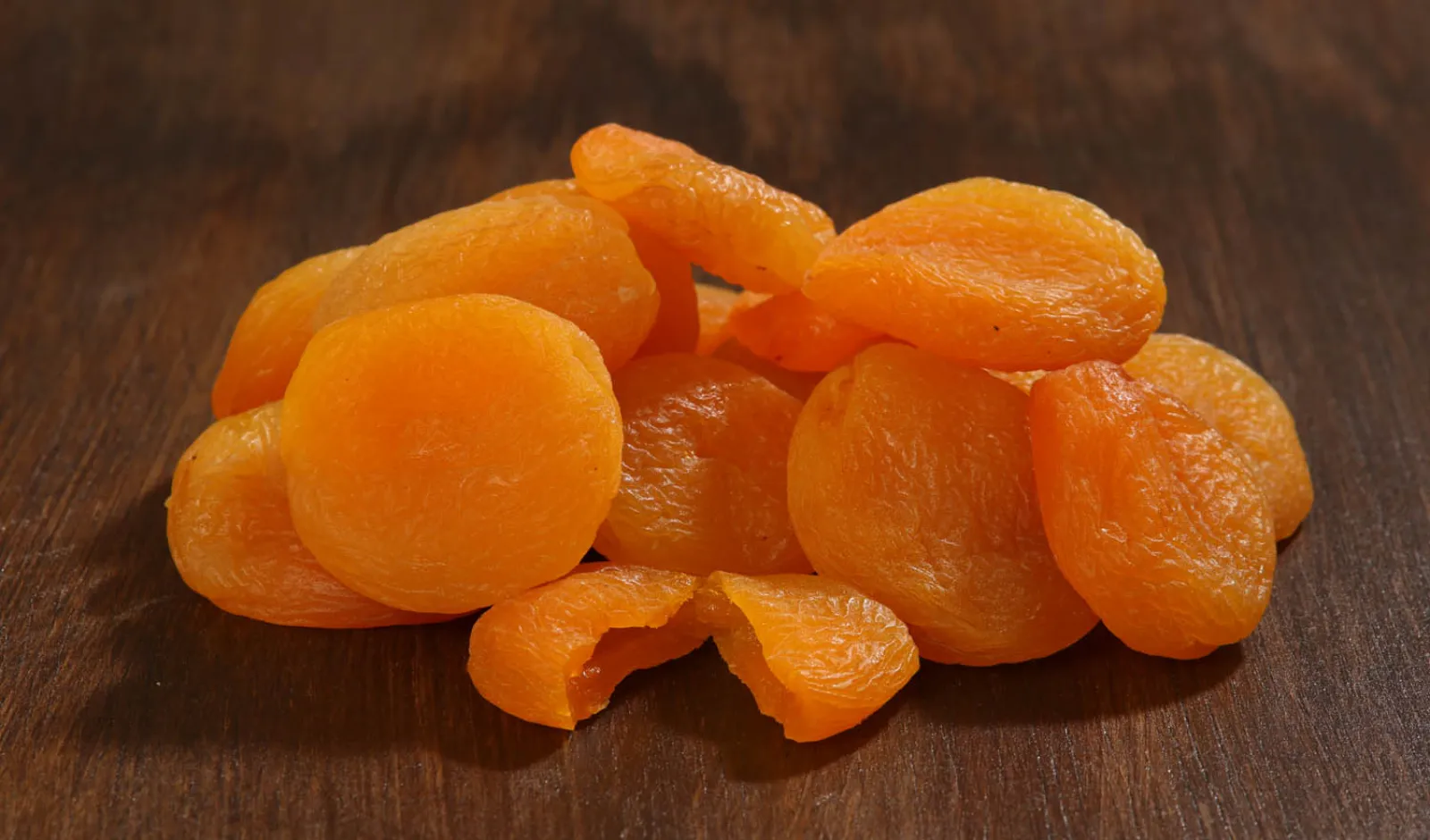 Bright orange dried apricots on a dark wooden surface